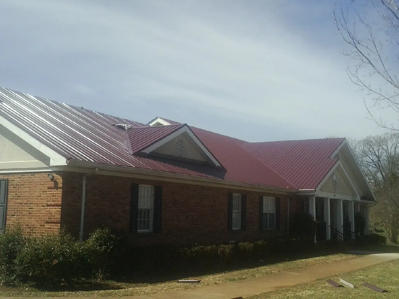 Red metal roof with gabled entries on a long brick building, from a Hail Damage Roof Repair job in Walnutport