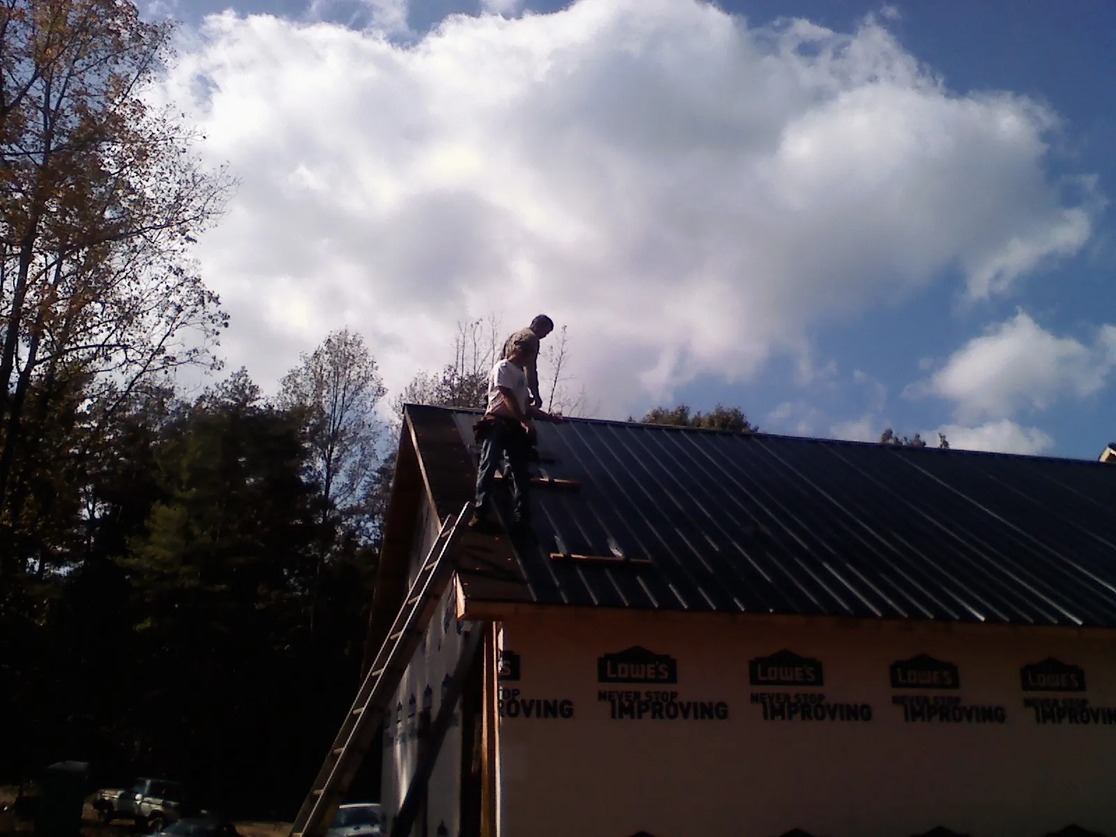 Roofer fastening dark metal panels high against a cloudy sky, from a Roof Inspection job in Walnutport