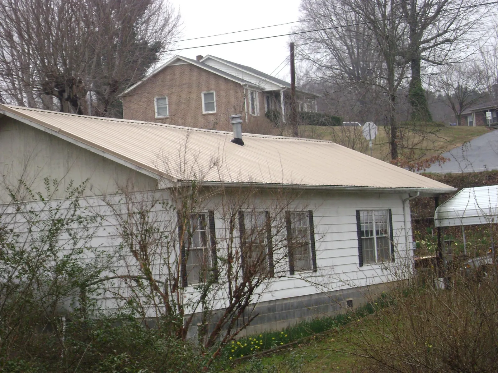 Tan metal roof on a white sided house set into a hillside — Commercial Roofing by Roofing Brothers in Walnutport